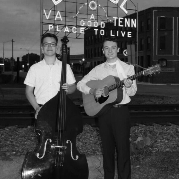 Zach McNabb holding a guitar and the Tennessee Esquires holding a cello in front of the Bristol, VA and TN sign