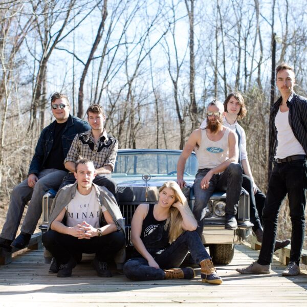 Members of the band (7 total) pose in front of old car on bridge